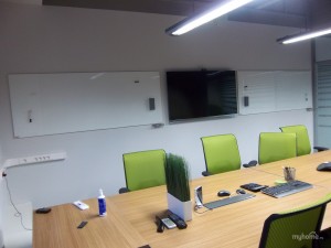 пустой кабинет с большим столом для совещаний, зелеными стульями и досками на всю стену